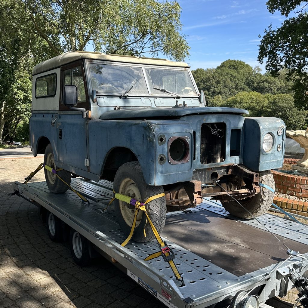 An old series 3 Land Rover in poor condition strapped to a trailer.